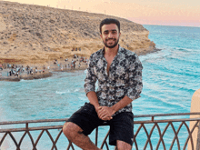 a young man sits on a railing overlooking the ocean