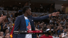 a man in a suit stands in front of a crowd at a basketball game between the raptors and pacers