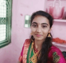 a woman in a pink and green dress is taking a selfie in front of a window