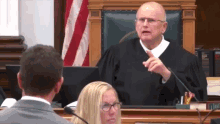 a man in a judge 's robe is speaking into a microphone in a courtroom while a woman watches .