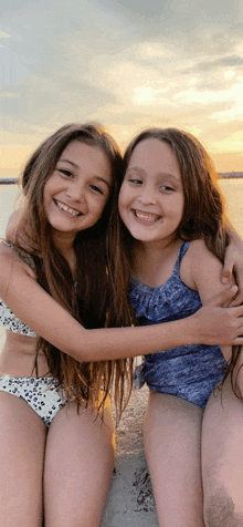 two young girls in bikinis are hugging each other on the beach