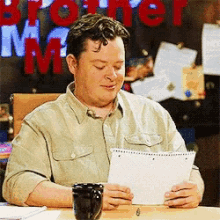 a man sits at a desk reading a piece of paper in front of a sign that says brother mr.