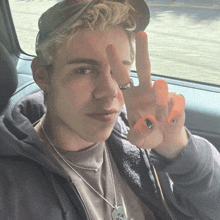 a young man wearing a hat and a necklace gives a peace sign