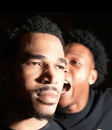 a man with a beard looks at the camera while another man screams in the background