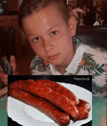 a boy is sitting at a table with a plate of sausages next to him