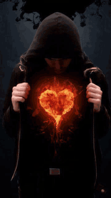 a man in a hooded jacket is holding a burning heart