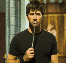 a man in a black t-shirt is holding a wand in his mouth