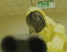 a man in a yellow suit and gas mask is pointing a gun at a fire exit sign