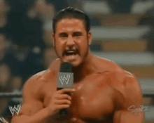 a shirtless wrestler is holding a microphone with a w logo on it