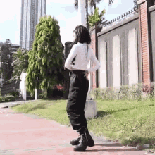 a woman in a white shirt and black pants is standing on a sidewalk in front of a fence .