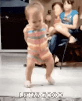 a little girl is dancing on a tiled floor while a woman holds a baby in a chair .