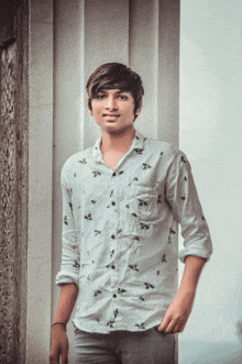 a young man leaning against a wall wearing a white shirt with flowers on it