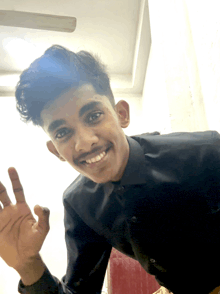 a young man in a black shirt smiles and waves his hand
