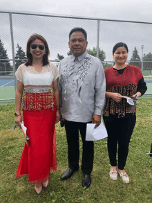 a man in a gray shirt is standing next to two women in red dresses