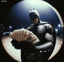 batman is holding a fan of money in his hand