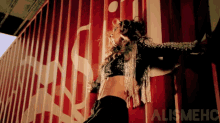 a woman dancing in front of a red wall that says alismehc on it