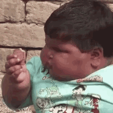 a young boy is eating a piece of food while wearing a blue shirt with cartoon characters on it .