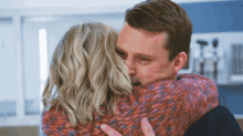 a man in a red sweater is hugging a blonde woman