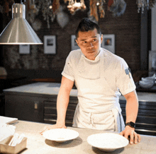 a man in a white apron stands in front of a counter with two bowls on it