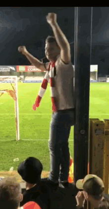 a man stands on a pole with his arms in the air in front of a soccer field with a coca cola sign in the background