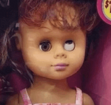 a close up of a doll with one eye closed in a pink dress .