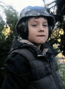 a young boy wearing ear muffs and a camouflage hat