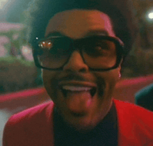 a man wearing glasses and a red jacket is sticking his tongue out .