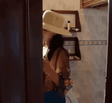 a woman in a hat is standing in a bathroom looking at her phone