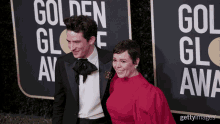 a man in a tuxedo and a woman in a red dress pose on a red carpet in front of a golden globe sign