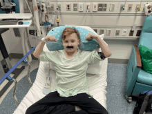 a boy in a hospital bed with a fake mustache on his face