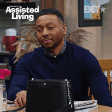 a man sits at a table with a laptop and a purse in front of a screen that says assisted living on it