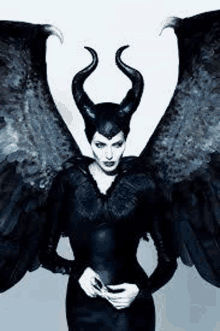 a woman dressed as maleficent with horns and wings is standing in front of a white background .