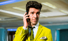 a man in a yellow suit and tie is talking on his cell phone