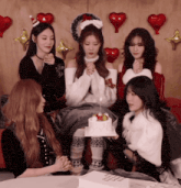 a group of girls are sitting around a table with a cake and balloons