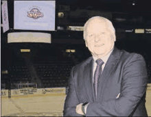 a man in a suit and tie is standing with his arms crossed in front of a computer screen .