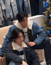 two men are sitting on a couch next to a christmas tree .