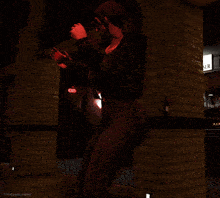 a woman is standing in front of a brick wall with a red exit sign in the background