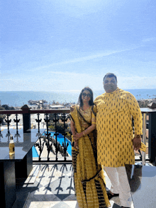 a man and a woman standing on a balcony with the ocean in the background