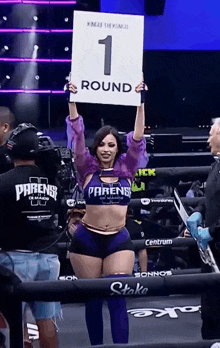 a woman holding a sign that says 1 round on it