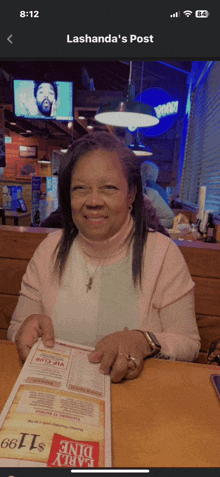 a woman sits at a table in a restaurant holding a menu and smiling for the camera