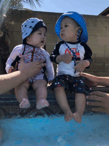 two babies are sitting next to each other in a pool and one is wearing a shirt that says ' a ' on it