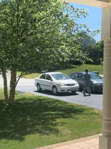 a white car is parked in a driveway next to a man