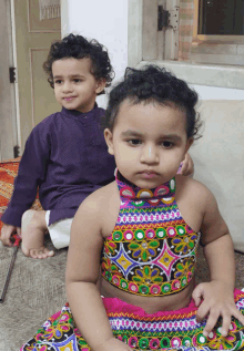 a boy in a purple shirt sits next to a little girl in a colorful dress