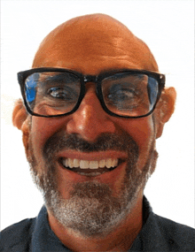 a bald man with glasses and a beard smiles