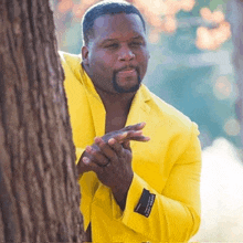 a man in a yellow suit is peeking out from behind a tree trunk .