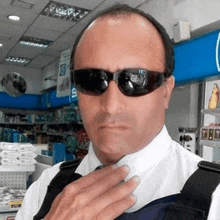 a man wearing sunglasses adjusts his tie in a store .