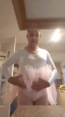 a man in a white leotard and pink tutu is standing in a kitchen