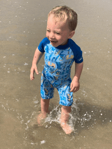 a little boy wearing a blue swimsuit is standing in the water on the beach