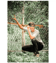 a young man squatting in front of a chain link fence with his arm outstretched