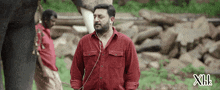 a man in a red shirt is standing in front of a pile of rocks with the letters xiii on the bottom